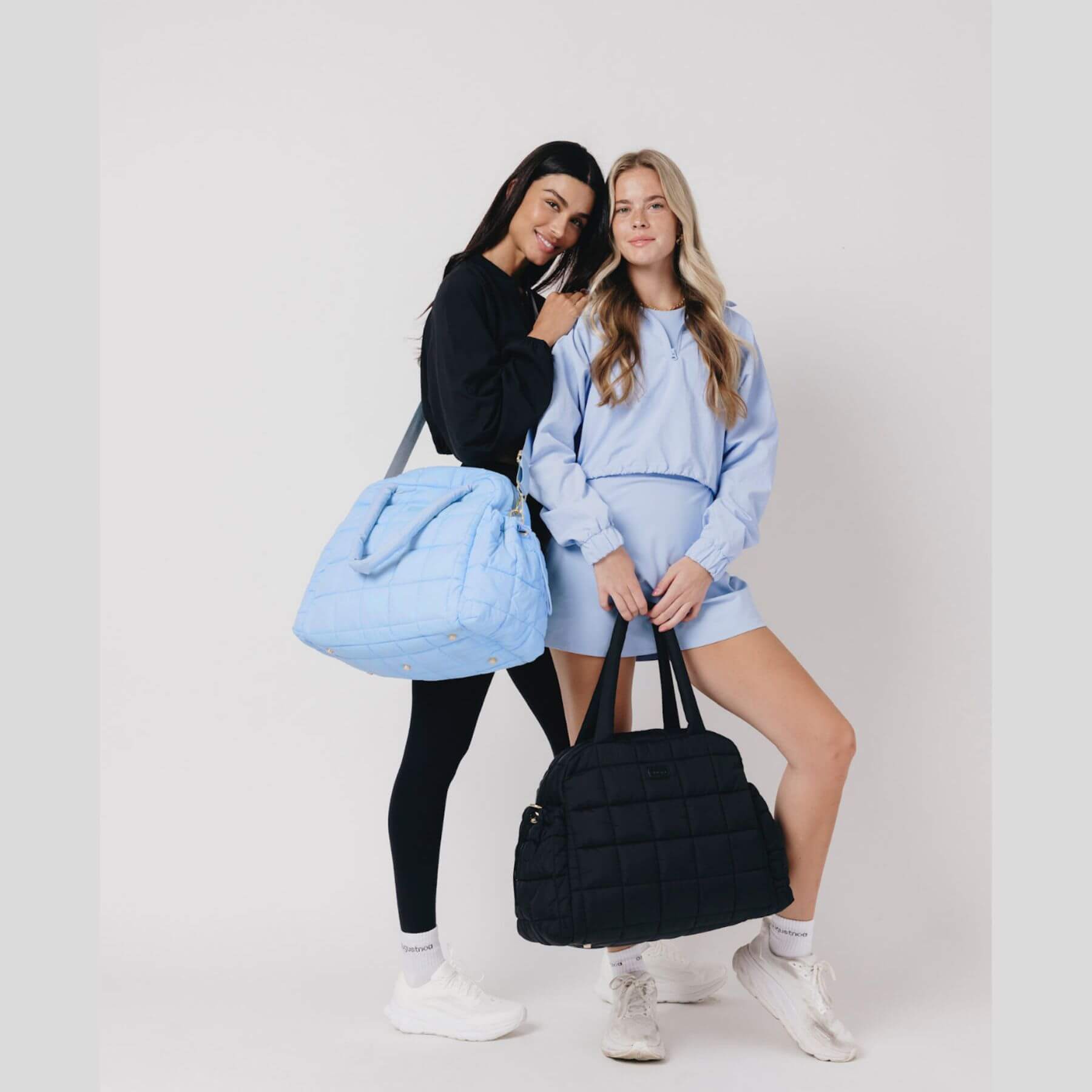 Two women holding a blue and a black augustnoa the weekender duffle bag