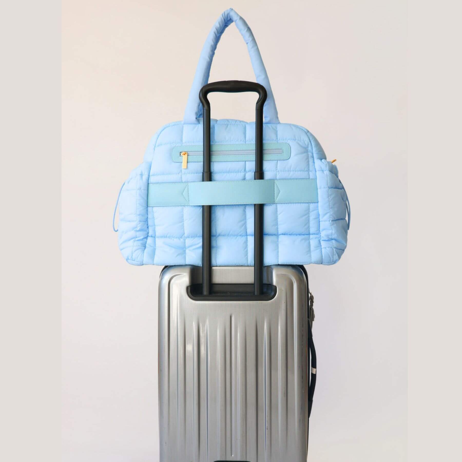 augustnoa the weekender duffle bag blue attached to a silver suitcase on a light gray background