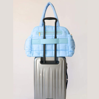 augustnoa the weekender duffle bag blue attached to a silver suitcase on a light gray background