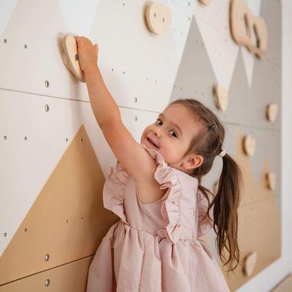 Child in a pink dress climbing on Wood and Hearts Indoor Climbing Wall