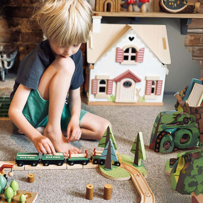 Child playing with Tender Leaf Wild Pines Train Set on the floor with a dollhouse in the background.