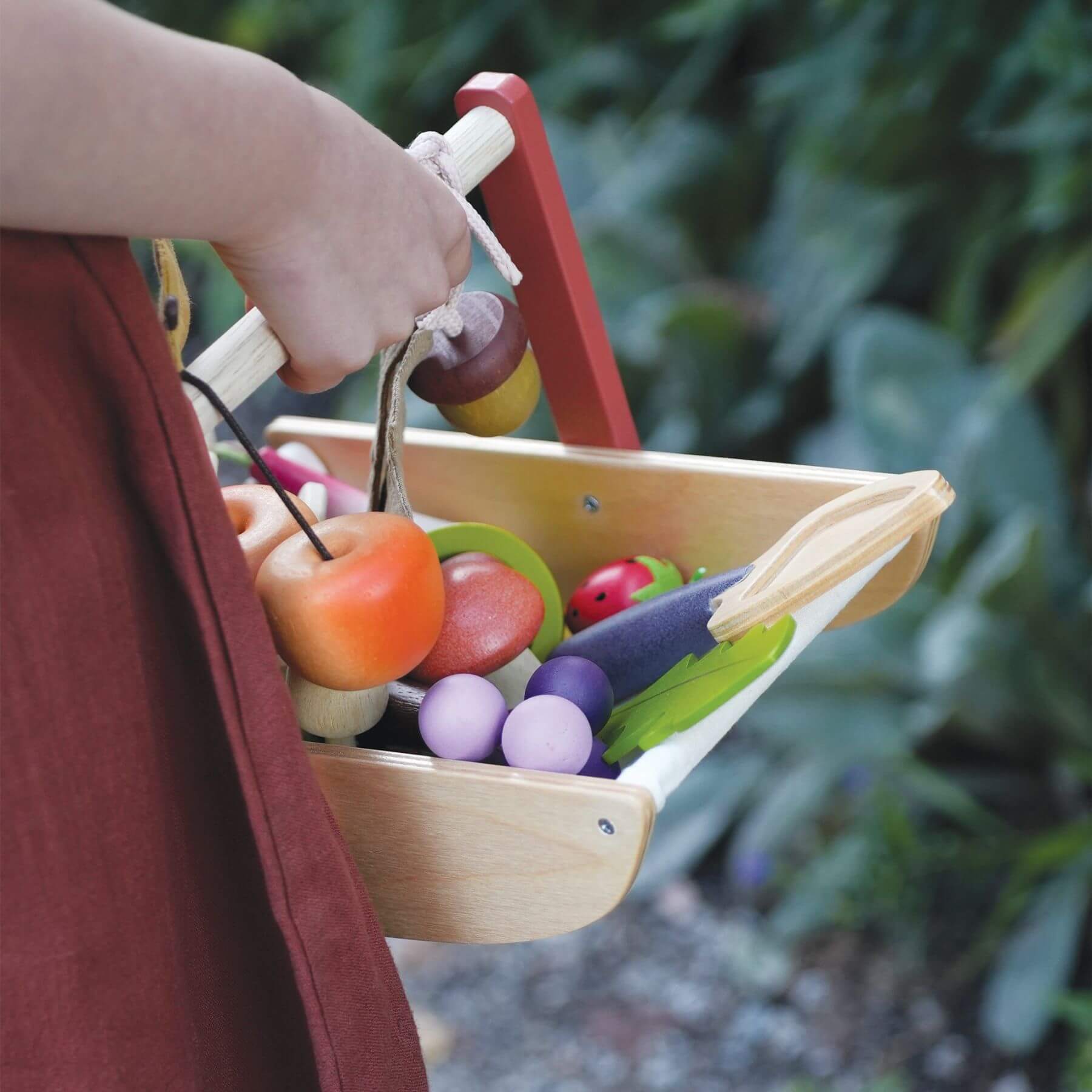 Child's hand holding Tender Leaf Wild Wood Foraging Trug against a blurred green outdoor background.