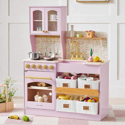 Tiny Land® Wooden Play Kitchen - Pink with Storage filled with toy food and dishes, staged on a rug against a white paneled wall.