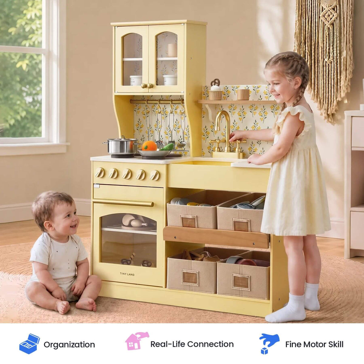 Tiny Land® Wooden Play Kitchen with Storage - Yellow, styled in a bright room with two children interacting with it. One young girl stands at the sink, and a baby boy sits on the floor nearby.