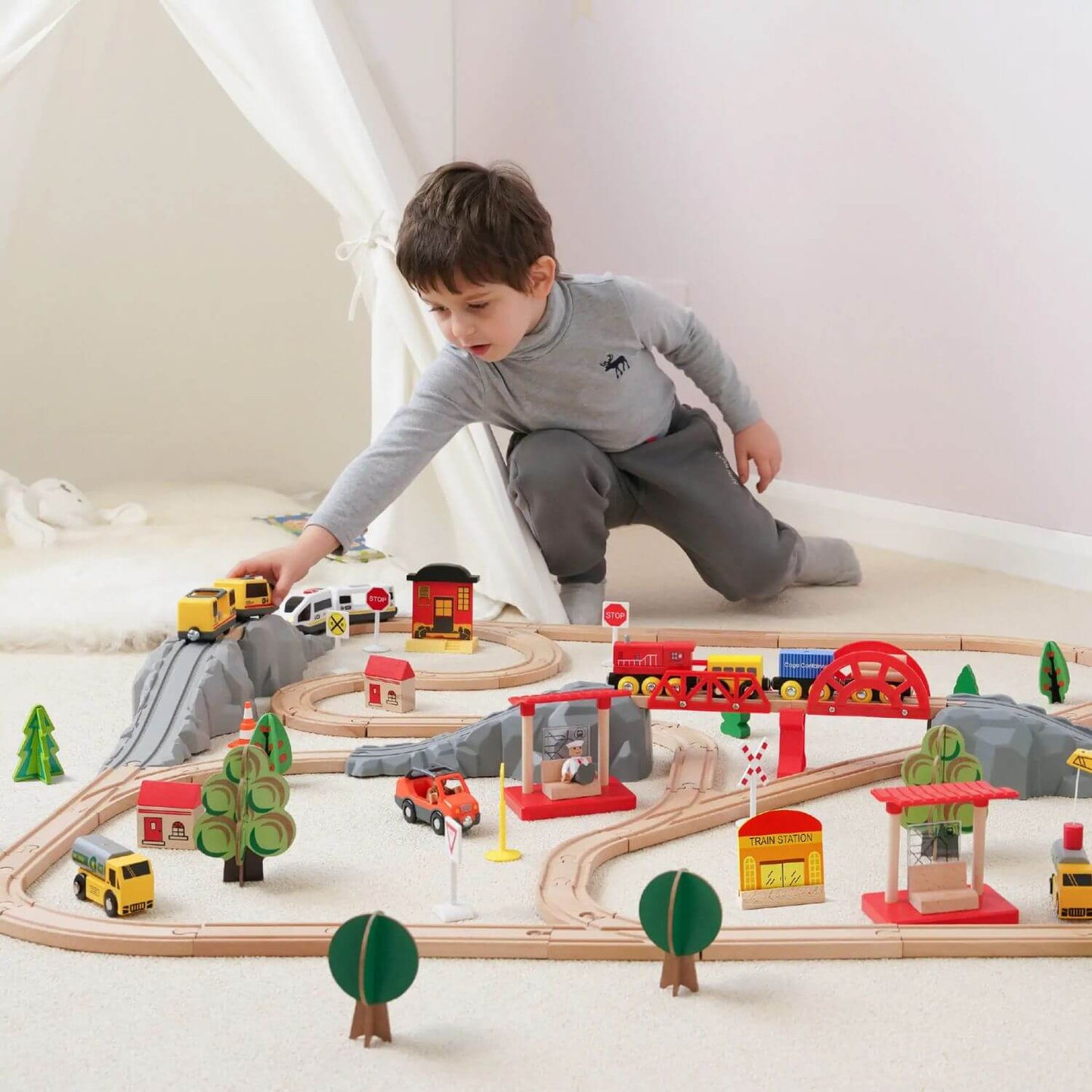 Child playing with a wooden train set on a white floor.