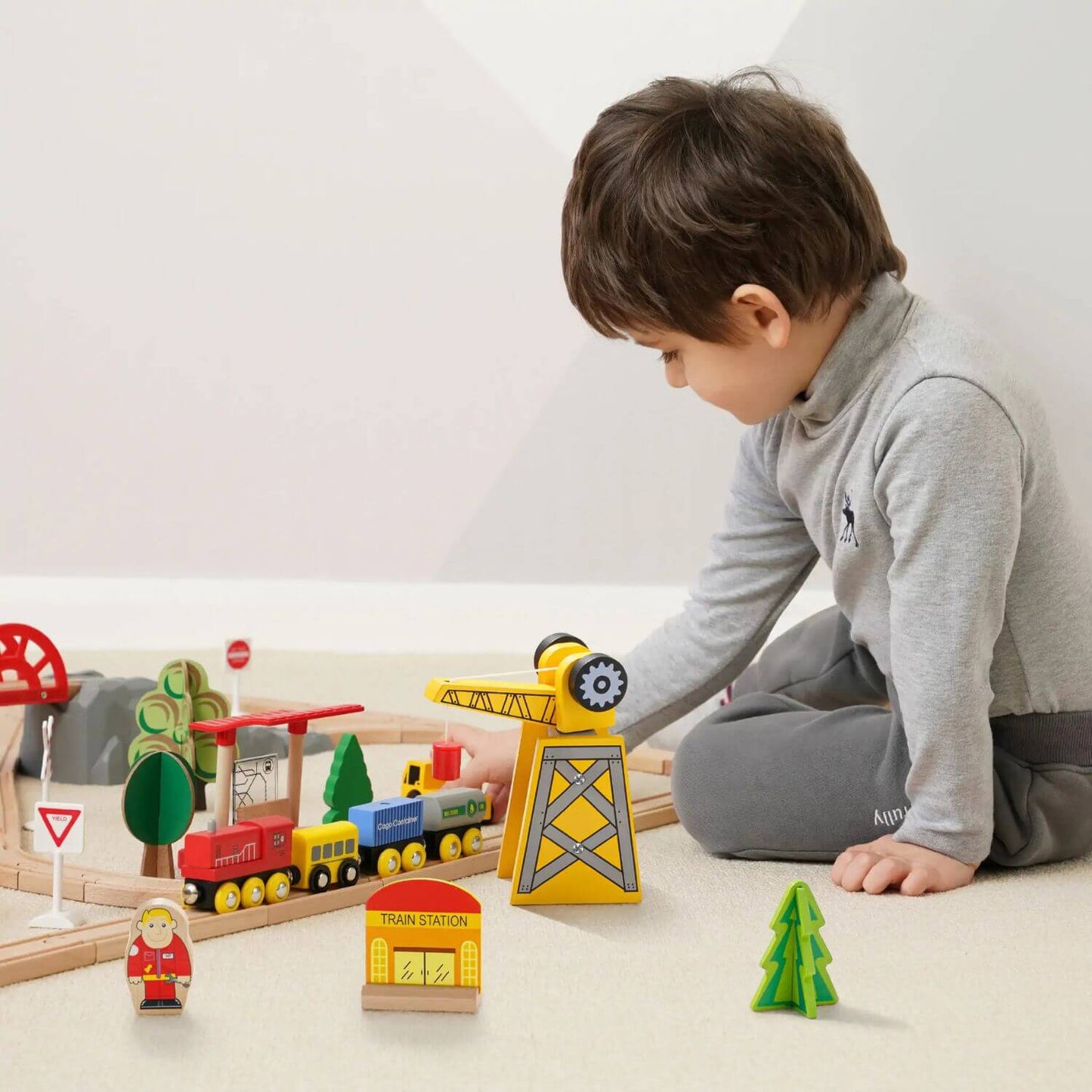 Child playing with a wooden train set on a light-colored floor.