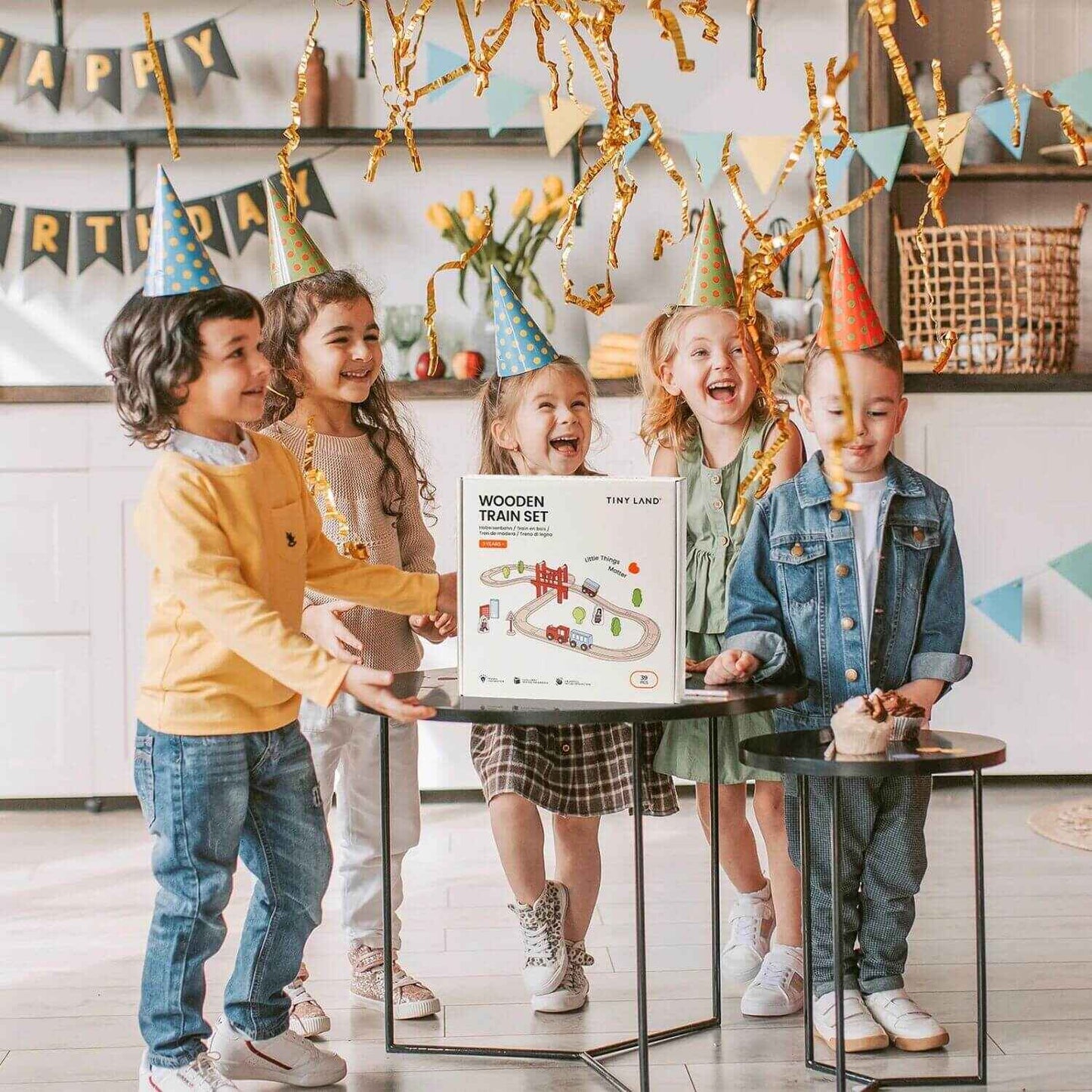 Children at a birthday party with a wooden train set box, surrounded by festive decorations.