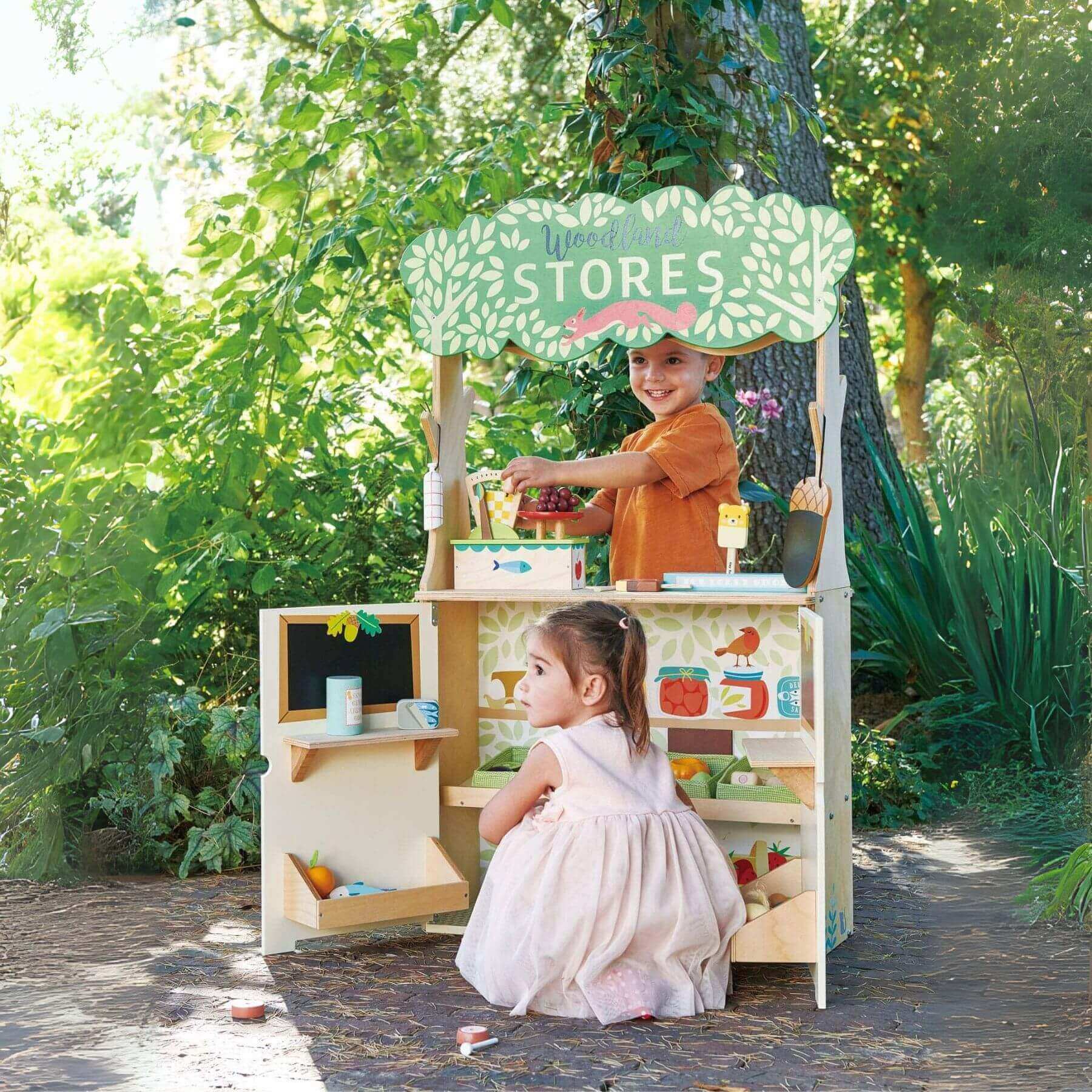 Two children playing with Tender Leaf Woodland Stores and Theater outdoors.