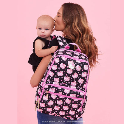 Woman holding a baby and wearing Cherry Blossoms Zealous Backpack against a pink background